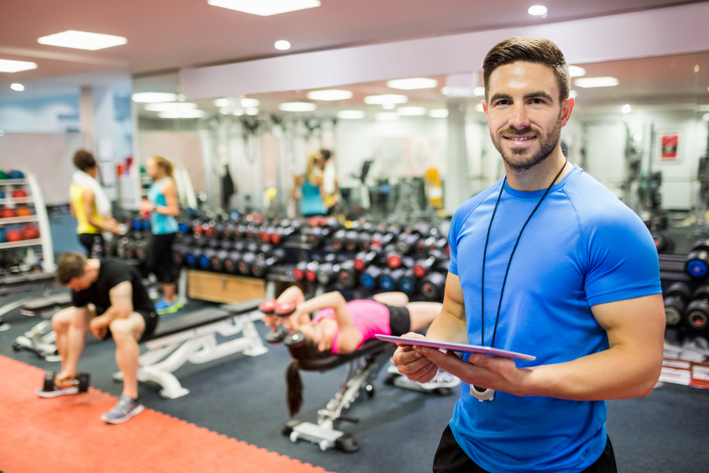 Handsome trainer using tablet in weights room